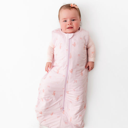 A baby lying down wearing a pink ballerina sleep sack