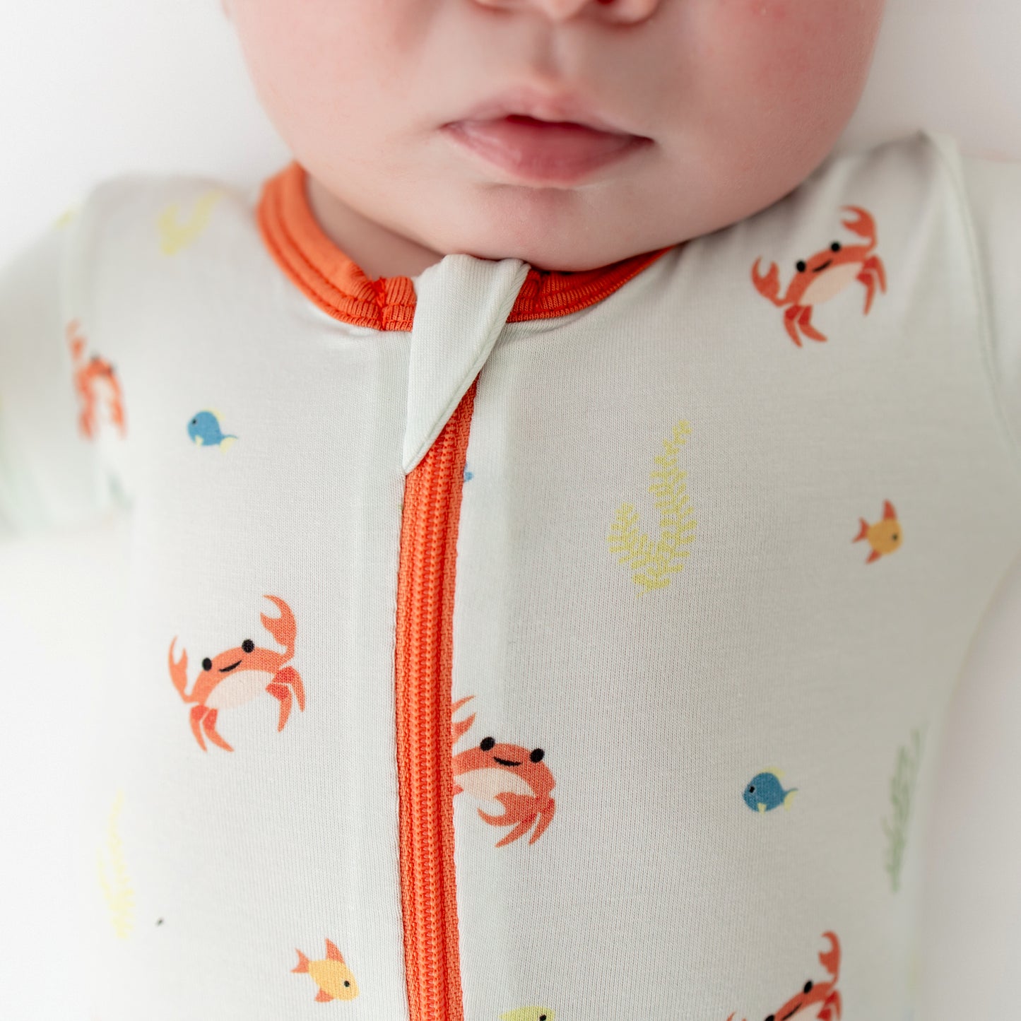 Close-up of a baby wearing a onesie with crab and fish patterns and orange zipper.