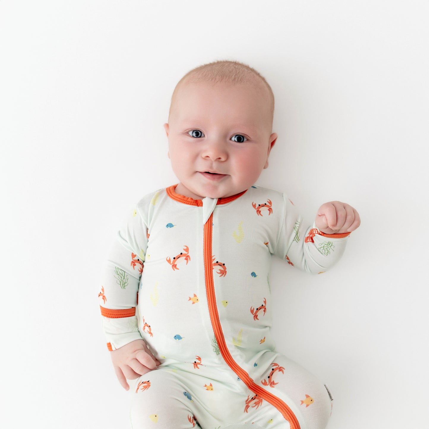 Baby wearing a bamboo footie with orange accents and animal prints on a colored background