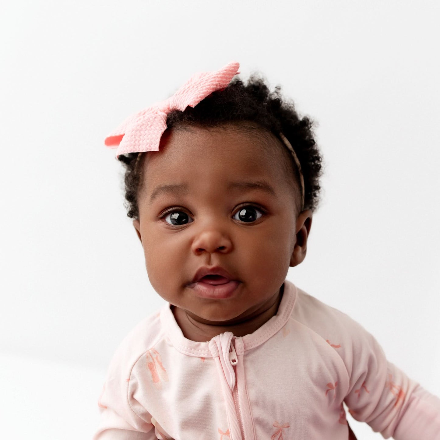 Baby wearing a pink outfit with a bow on a white background