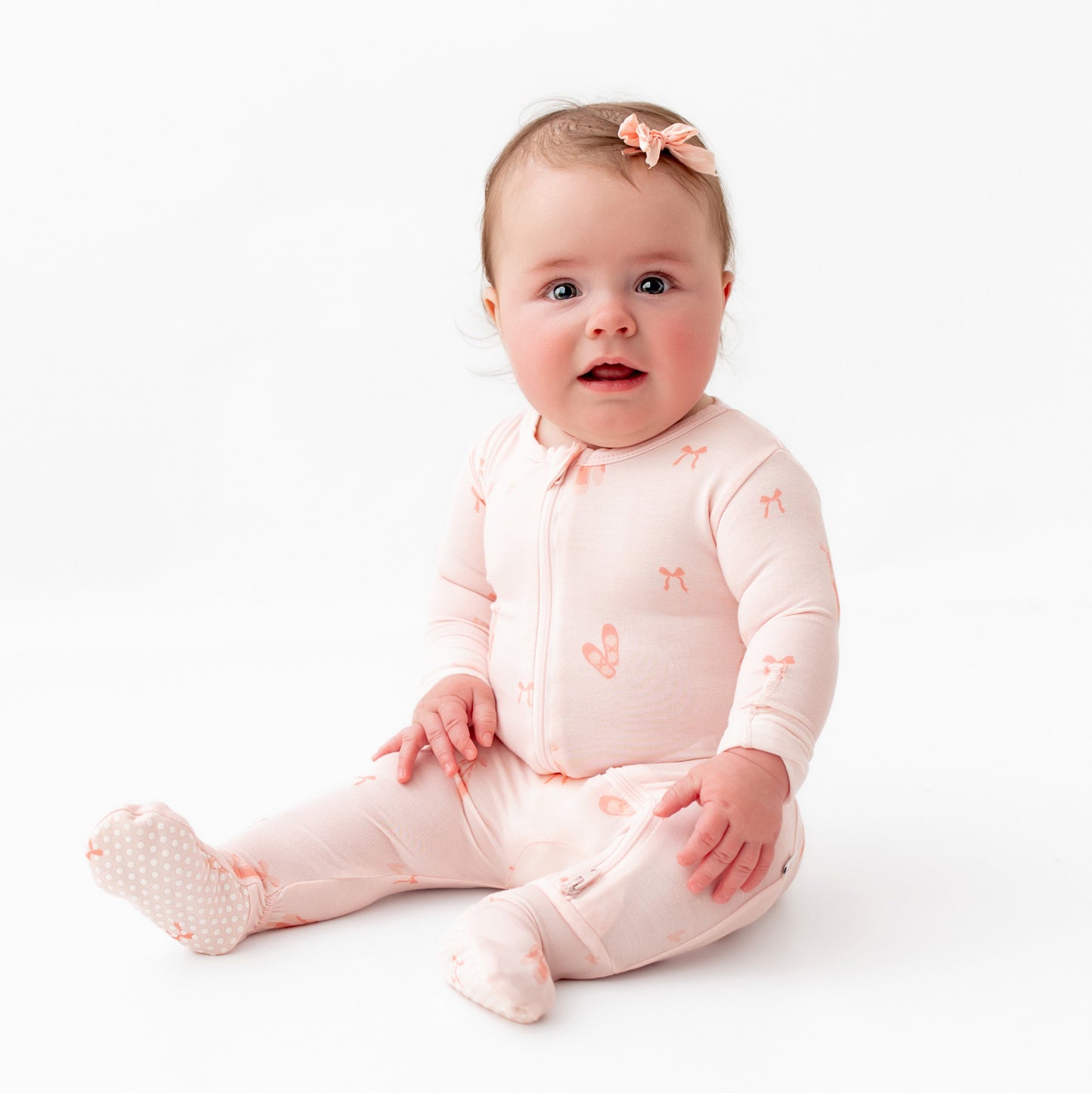 A sitting baby wearing a pink ballerina zippered footie