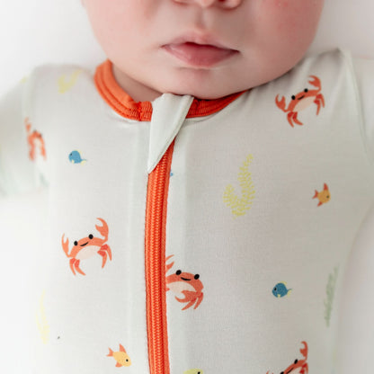 Close-up of a baby wearing a onesie with crab and fish patterns and orange zipper.