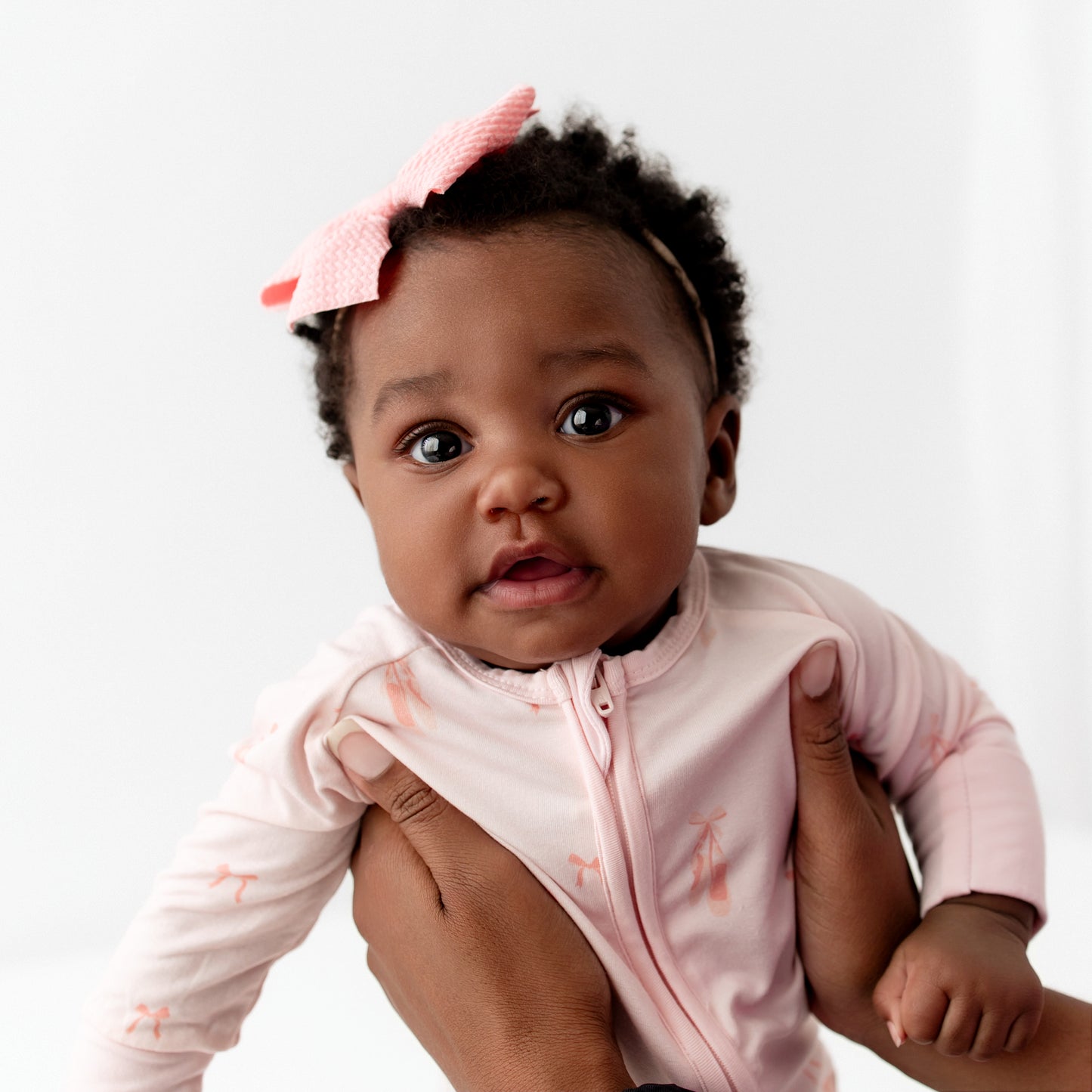 Baby in a pink outfit with a headband on a white background