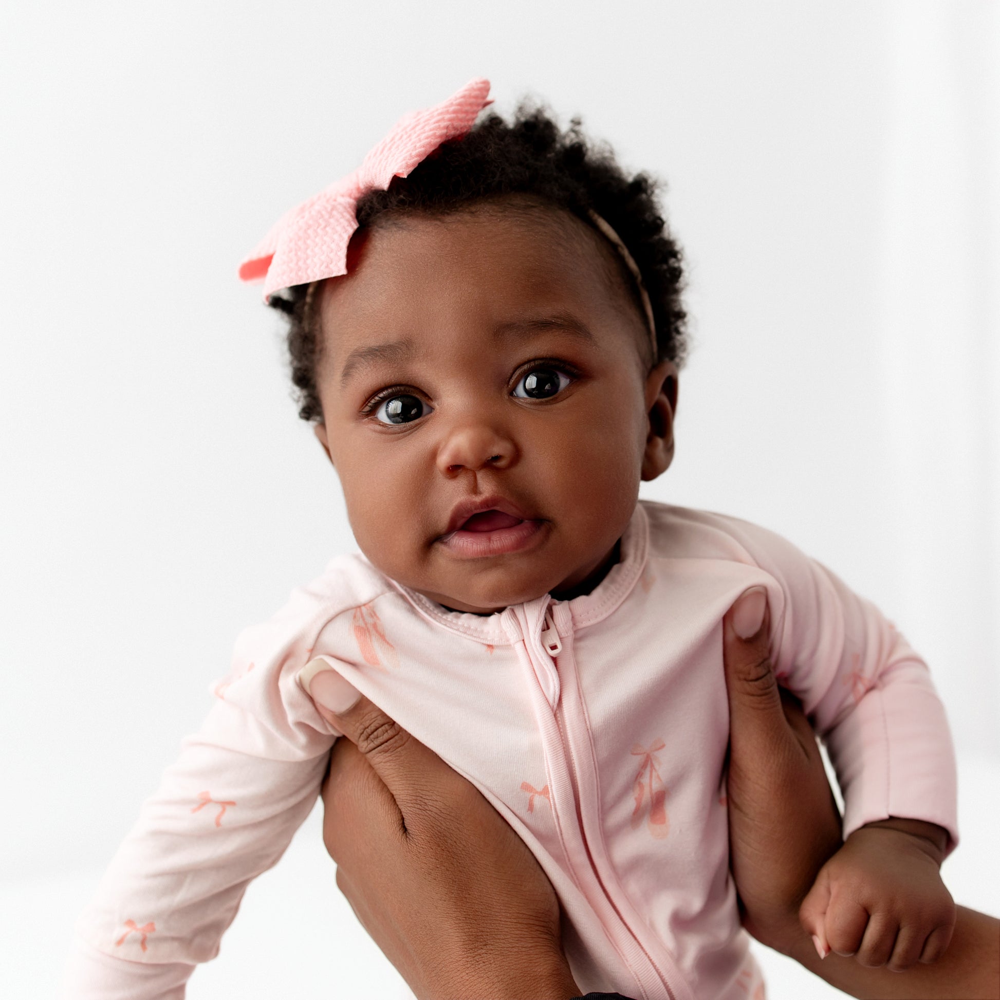 Baby in a pink outfit with a headband on a white background